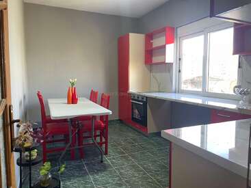 This kitchen features red and white cabinets, green tiled floor, a white table with red chairs, large window, plants, and modern decor with natural light.