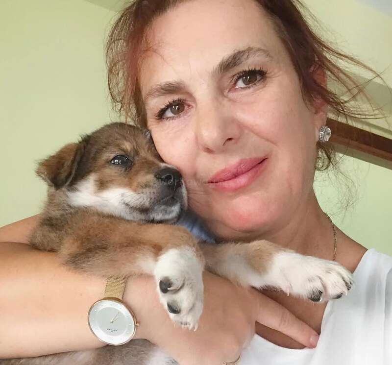 A woman lovingly cuddles a small brown and white puppy, both appearing very content and close. She’s wearing a watch and smiling warmly at the camera.