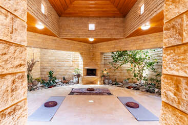 Cette pièce paisible est dotée de murs en pierre, d'un plafond en bois, de tapis de yoga et de coussins de méditation, d'un jardin intérieur, d'une lumière naturelle et d'une atmosphère sereine, idéale pour la détente ou la méditation.
