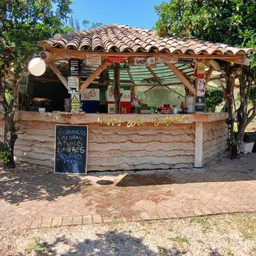 Se trata de un bar rústico al aire libre con techo de tejas, rodeado de árboles. En una pizarra se enumeran las diferentes cervezas. El ambiente es relajado, soleado y acogedor.