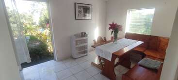 A imagem mostra uma sala aconchegante com uma mesa e cadeiras, com uma grande janela, uma lareira e uma estante de livros, evocando uma sensação de calor e conforto. A sala é bem iluminada e convidativa.