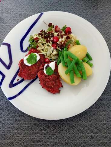 A beautifully plated meal featuring beetroot patties with cream, potatoes with green beans, and a fresh salad with greens, cabbage, strawberries, and edible flowers.