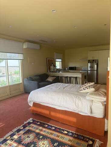 Ce studio confortable dispose d'un lit, d'un tapis coloré, d'un petit canapé et d'un coin cuisine avec des tabourets de bar. De grandes fenêtres offrent une lumière naturelle et une vue sur le jardin.