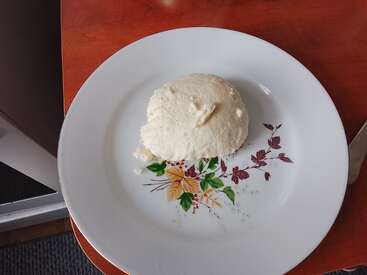 Ein weißer, runder Haufen Ugali liegt auf einem dekorativen weißen Teller mit Blumenmuster, der auf einem Holztisch steht und servierfertig ist.