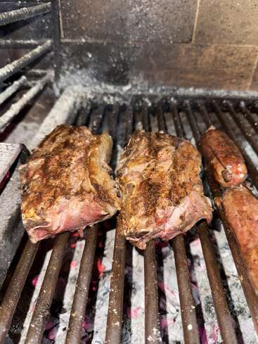 Dicke, saftige Rindfleischstücke und Würstchen brutzeln auf einem Grill über heißer Holzkohle, während glühende Kohlen und Grillstreifen das köstliche Barbecue unterstreichen.
