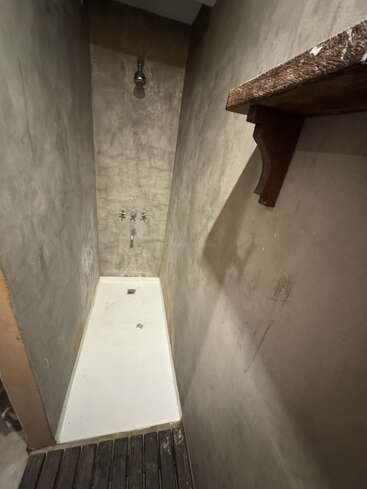 Cette photo montre un petit espace douche au style minimaliste, avec des murs en béton, un receveur de douche blanc, un plancher en lames de bois, une étagère rustique en bois et des installations apparentes.