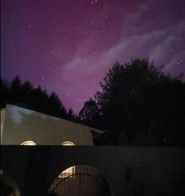 A imagem mostra uma cena noturna serena com um edifício com janelas em arco, árvores e um céu roxo vibrante pontilhado de estrelas.