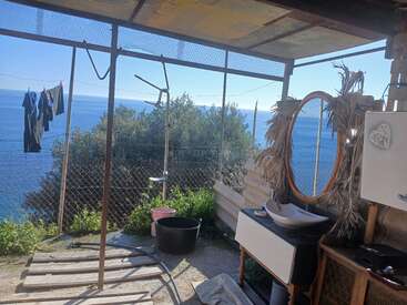 Cette image montre une salle de bain et une buanderie rustiques en plein air, avec une vue imprenable sur la mer, des meubles en bois, un lavabo, une douche, un miroir, une corde à linge et une végétation luxuriante.