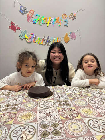 Three people sit at a decorated table for a birthday celebration. A chocolate cake is in front of them, and cheerful decorations and smiles fill the scene.