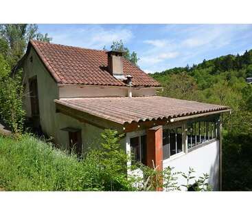 This image shows a rustic house with a red-tiled roof, chimney, enclosed porch, surrounded by greenery and trees, against a clear blue sky. Peaceful setting.