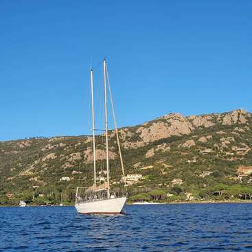 The image depicts a serene scene of a white sailboat floating on a tranquil body of water, with a majestic mountain range serving as a picturesque backdrop.