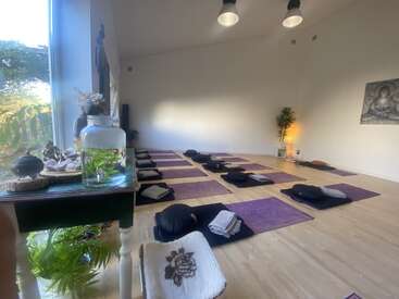 Ein ruhiges Yoga-Studio mit lila Matten, Meditationskissen, Pflanzen und sanftem Tageslicht. Eine friedliche Atmosphäre mit minimalistischer Einrichtung, die Entspannung, Achtsamkeit und innere Ruhe fördert.