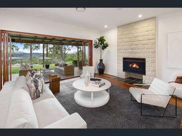 Essa aconchegante sala de estar apresenta uma lareira moderna, móveis claros, uma mesa de centro redonda e se abre perfeitamente para um convidativo pátio externo com vistas panorâmicas.