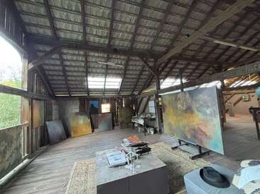 Il s'agit d'un atelier d'art spacieux et rustique, doté d'un plafond en bois. De grandes peintures abstraites, du matériel artistique et la lumière naturelle y créent une atmosphère créative, inspirante et détendue.