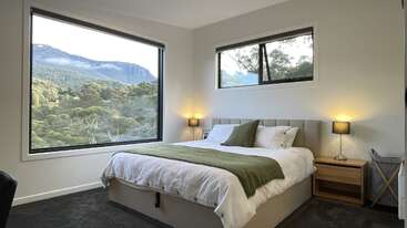 Este quarto aconchegante tem uma cama grande com detalhes em verde, mesinhas de cabeceira com abajures e uma vista deslumbrante das montanhas pelas janelas amplas, criando um ambiente sereno.