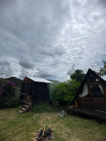Dos pequeñas cabañas de madera se asientan en un patio cubierto de hierba bajo un espectacular cielo nublado. Hay leña en el suelo, lo que sugiere una acogedora reunión al aire libre.