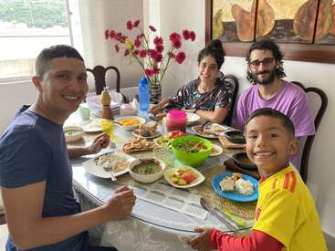 A smiling family of four sits around a table enjoying a colorful, delicious meal. The atmosphere is cheerful, with vibrant flowers and cozy home décor.