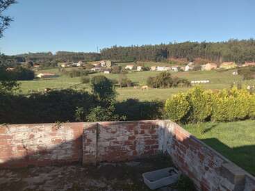 Un patio de ladrillo desgastado por el tiempo da a un paisaje verde donde pastan las vacas. Pequeñas casas salpican las colinas onduladas, rodeadas de un denso bosque bajo un cielo azul y despejado.