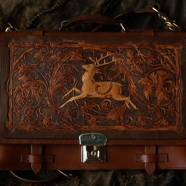 This is a beautifully crafted leather bag with intricate carvings of a stag surrounded by floral patterns, featuring rich brown hues and a metallic clasp.