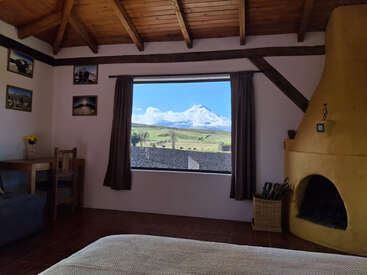 A imagem mostra um quarto aconchegante com uma grande janela que oferece uma vista panorâmica de uma montanha coberta de neve, complementada por uma lareira e uma cama confortável.