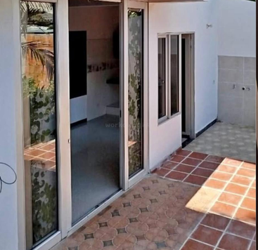 This image shows a modern patio area with glass sliding doors, patterned floor tiles, white walls, a small window, and a partially shaded outdoor space.