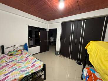 A tidy bedroom with tiled floors has a double bed, colorful bedding, bunk beds, large dark wardrobes, a wooden ceiling, and a person near the door.