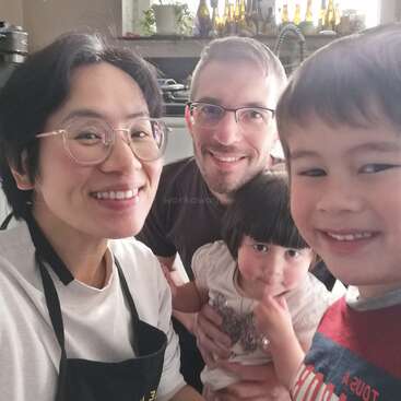 L'image représente une famille de quatre personnes dans une cuisine, la mère portant un tablier et le père tenant un jeune enfant, tandis que l'enfant plus âgé se tient à côté d'eux.