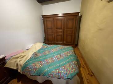 Esta imagen muestra un dormitorio pequeño y acogedor con un armario de madera, una cama doble cubierta con una manta de estampado colorido, suelo de madera y una decoración sencilla.