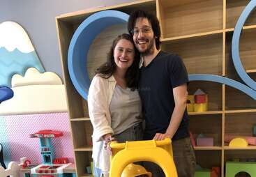 Un couple heureux se tient dans une salle de jeux colorée, souriant chaleureusement. Derrière eux, des étagères remplies de jouets et de décorations ludiques créent une atmosphère joyeuse et familiale.