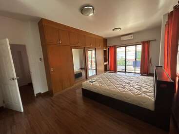 Cette chambre spacieuse dispose d'un grand lit, d'un plancher en bois, d'armoires encastrées en bois avec des miroirs, de rideaux rouges, d'un accès au balcon, de l'air conditionné et d'une lumière naturelle abondante.
