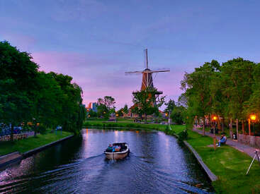 The image depicts a serene canal scene with a boat, lush greenery, and a windmill in the background, evoking a peaceful atmosphere.