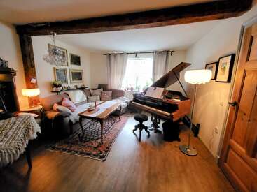 Esta aconchegante sala de estar apresenta um piano de cauda, um sofá de estilo vintage, uma mesa de centro de madeira, iluminação aconchegante, arte emoldurada, plantas domésticas e um tapete decorativo, criando uma atmosfera acolhedora.