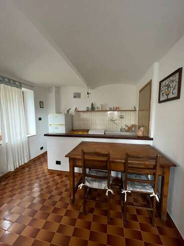 Dieses Bild zeigt eine kleine, gemütliche Küche mit braunen, karierten Fliesen, einem Holztisch und Stühlen, einem weißen Kühlschrank, einer gefliesten Aufkantung und schlichtem Dekor an den Wänden.