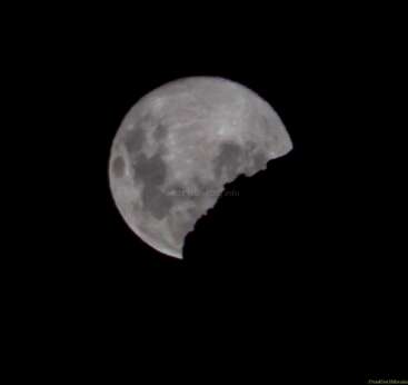 A imagem mostra uma lua cheia brilhante em um céu escuro, parecendo que uma grande mordida foi dada em seu lado inferior direito.