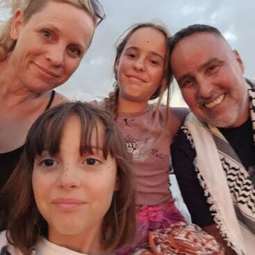 Une famille souriante de quatre personnes prend un selfie en gros plan en plein air au coucher du soleil. Deux adultes et deux enfants profitent joyeusement d'un moment privilégié.