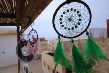 Atrapasueños colgantes con plumas de colores, incluidos el verde y el rosa, se balancean en un balcón con vistas a edificios y a un cielo lejano y brumoso en un día tranquilo.