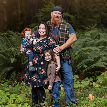 Uma família feliz de quatro pessoas posa ao ar livre, cercada por plantas e samambaias verdes exuberantes. Eles estão sorrindo, vestidos com roupas quentes e irradiam calor e união na natureza.