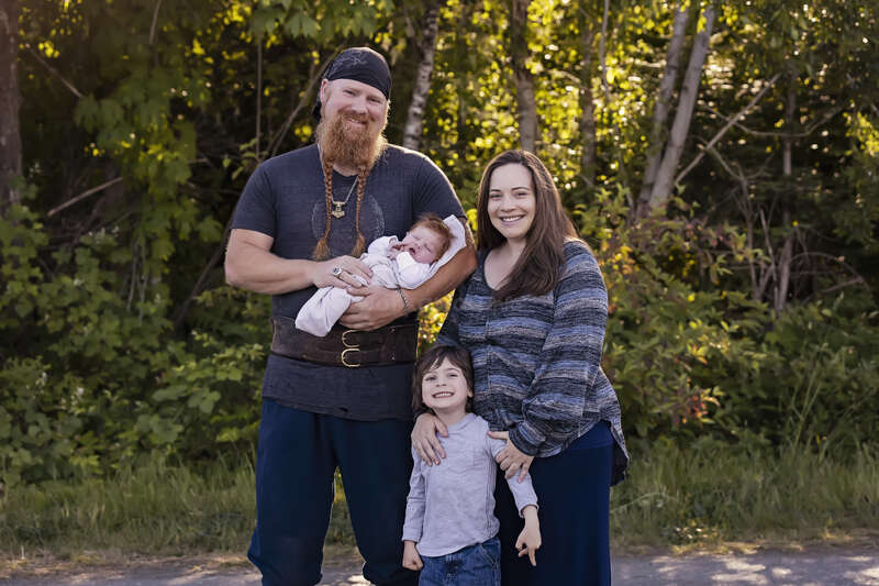 A imagem retrata uma família de quatro pessoas posando para uma foto, com dois adultos e duas crianças, mostrando seu vínculo afetivo e expressões alegres. A felicidade da família é evidente na imagem.