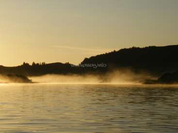 The image depicts a serene lake scene at sunrise or sunset, with a misty atmosphere and a hill in the background, set against a warm and golden sky.
