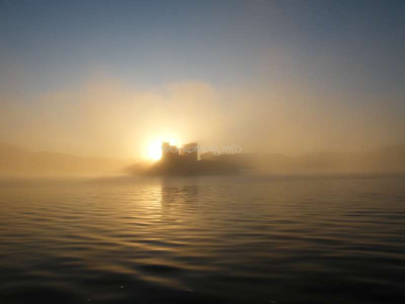 The image depicts a serene scene of a body of water at sunrise or sunset, with a building in the distance and a subtle watermark.