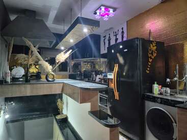 This modern kitchen features black appliances, gold accents, and unique lighting. Decorative plants and wall art add a stylish, cozy atmosphere to the contemporary space.