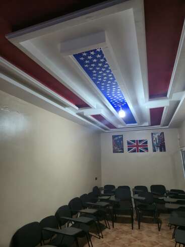 This image shows a classroom with empty black chairs, American-themed ceiling décor, posters, and a British flag on the wall, creating a language or cultural learning environment.