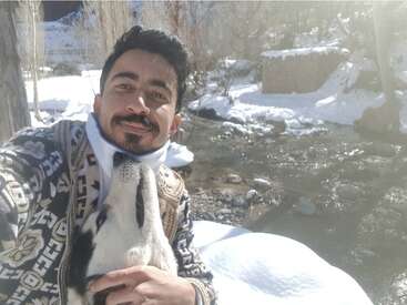 Un homme prend un selfie joyeux avec son chien au bord d'une rivière enneigée. La lumière du soleil scintille sur la neige, créant une scène hivernale paisible et joyeuse.