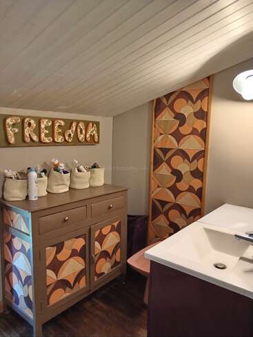 This cozy bathroom features a slanted ceiling, geometric-patterned cabinets, a modern sink, organizer baskets, and a “FREEDOM” sign for a unique, artistic touch.
