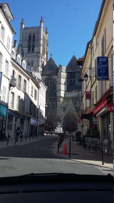 Das Bild zeigt eine ruhige Straßenszene mit einer majestätischen Kathedrale in der Mitte, flankiert von Gebäuden und einem klaren blauen Himmel darüber.