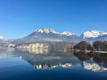 L'image représente une scène de lac sereine avec des montagnes enneigées en arrière-plan, avec un ciel bleu clair et une atmosphère tranquille.