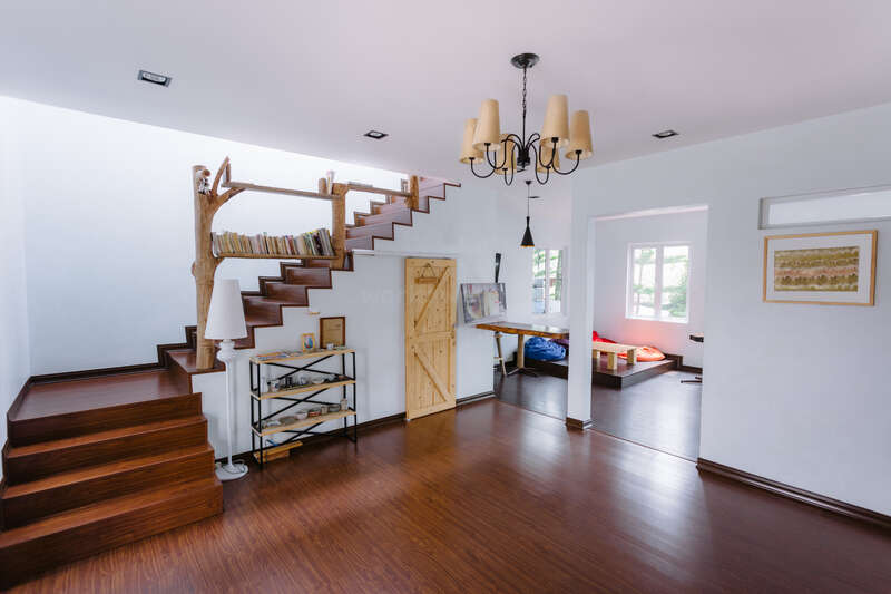 Das Bild zeigt einen modernen, offenen Raum mit weißen Wänden und dunklen Holzböden, der mit einer Treppe, einem Kronleuchter und verschiedenen Möbelstücken ausgestattet ist.