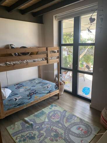 Dieses gemütliche Kinderzimmer verfügt über Etagenbetten aus Holz, verspielte Bettwäsche, eine bunte Spielmatte mit Straßen, große Fenster, eine Hängematte draußen sowie diverses Spielzeug und Deko.