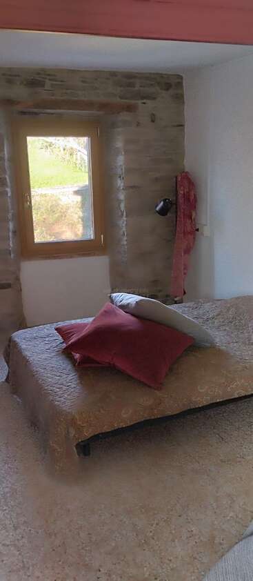 Cette chambre confortable comprend un lit orné d'oreillers marron et rouges, un mur rehaussé de pierres, une fenêtre en bois, une lampe et une vue dégagée sur l'extérieur.