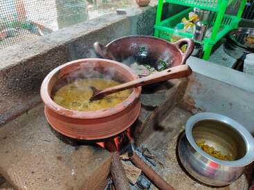 This image shows traditional Indian cooking on a wood fire stove, with clay pots simmering delicious food, a wooden ladle, and kitchen utensils nearby. Cozy atmosphere prevails.
